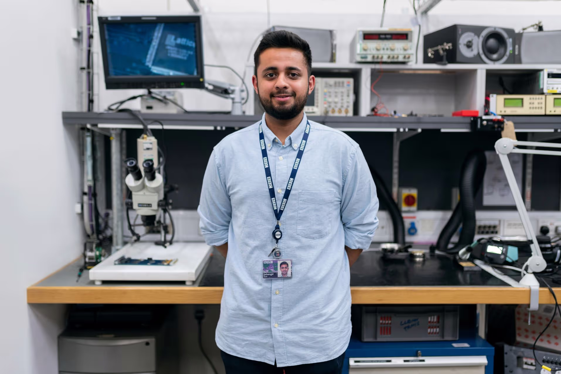 Chercheur de laboratoire souriant debout devant un banc d'essai et de tests en microéletronique